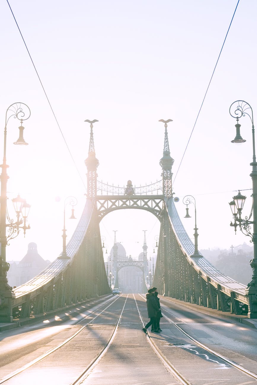 pedestrians crossing bridge with tramway rails against sunshine