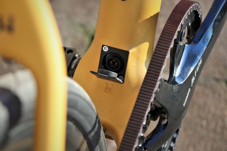 Close de um plugue elétrico na frente de uma bicicleta amarela.