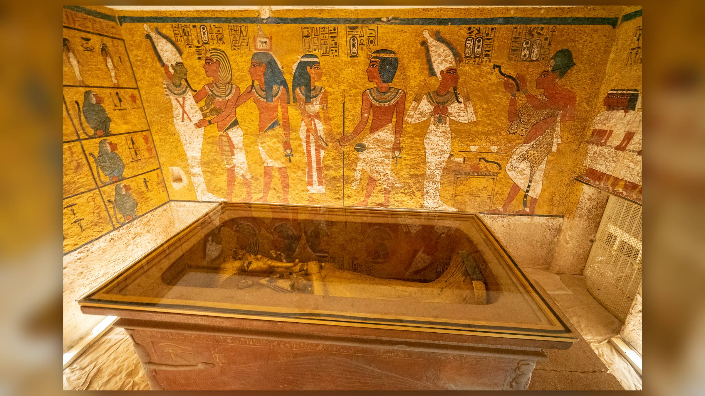 Uma foto do túmulo do faraó Tutancâmon no Vale dos Reis em Luxor.  O caixão fica no centro da sala, com pinturas egípcias nas paredes.
