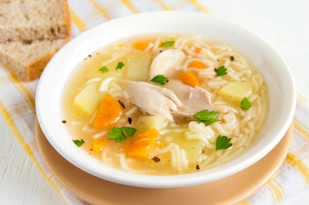 Sopa de galinha com macarrão e legumes em tigela branca