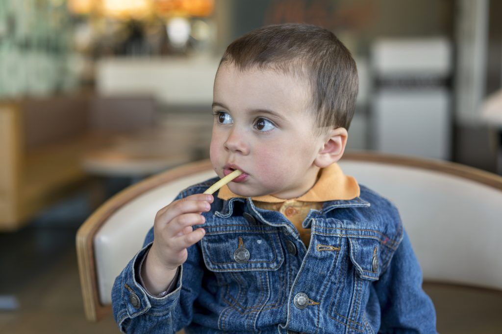 menino bonitinho sentado no café comendo saborosas batatas fritas