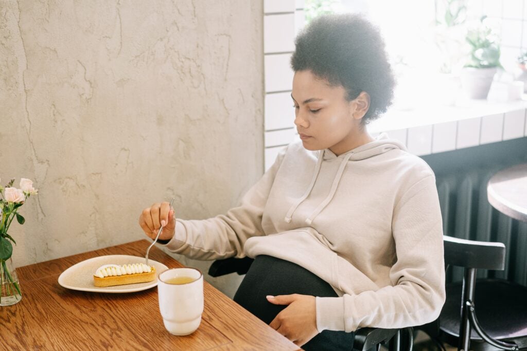 Mulher grávida comendo uma fatia de torta em uma mesa