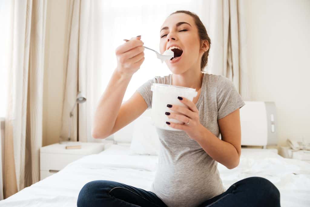 jovem grávida sentada na cama e comendo sorvete